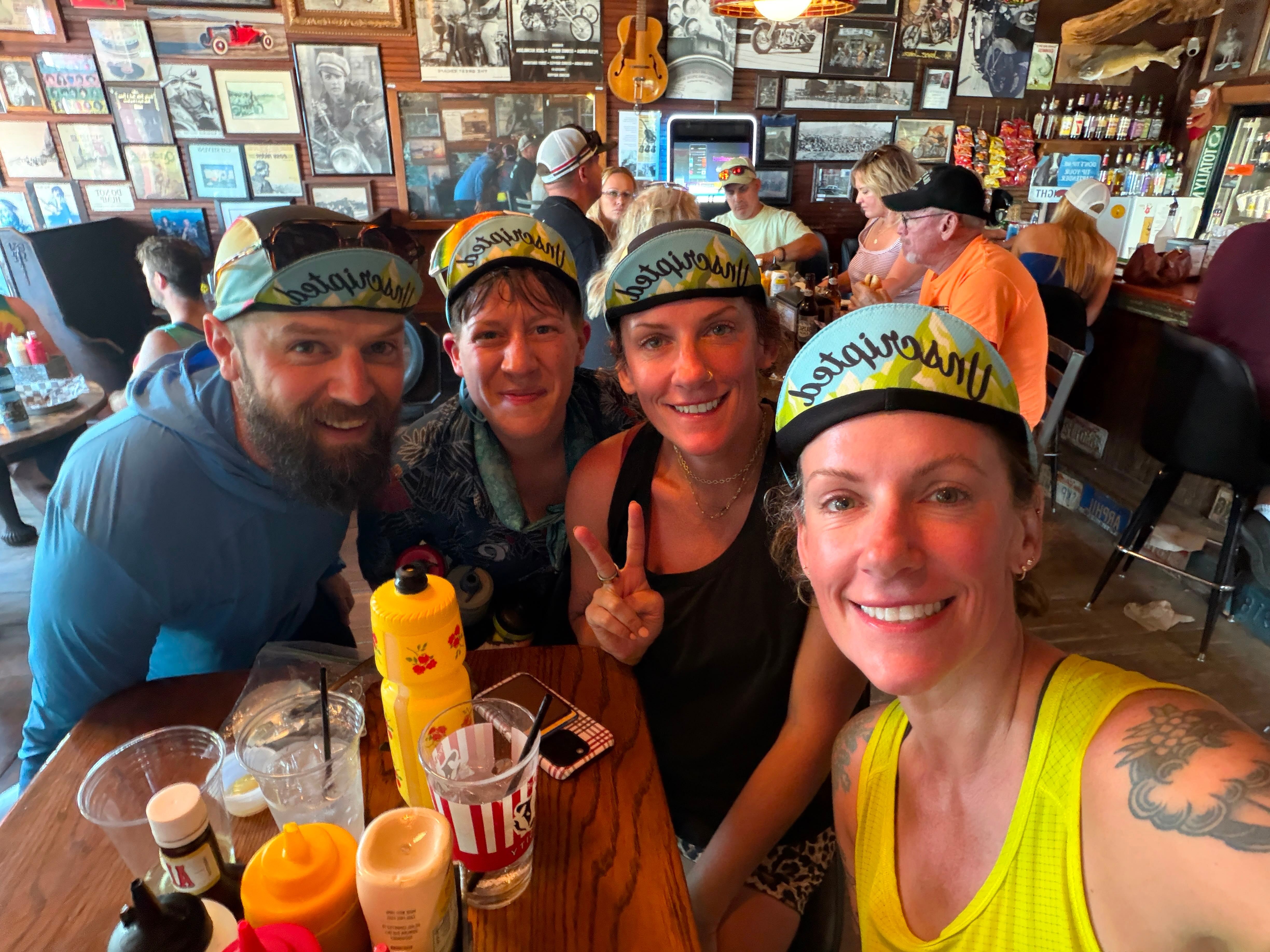 A group of riders in Lil Drifty caps crowded around a tavern table covered in drinks